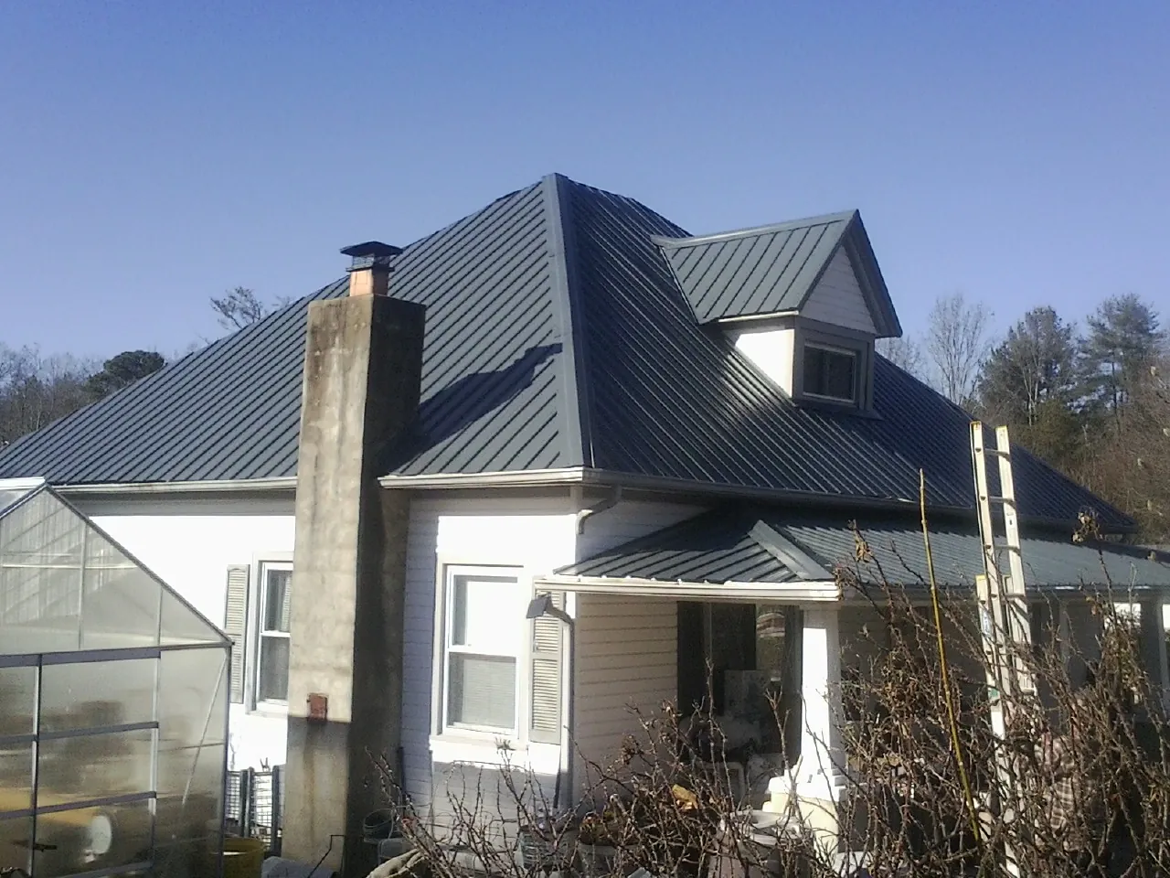 Dark blue standing seam metal roof on a white farmhouse with dormer — Slate & Tile Roof Repair by Roofing Brothers in Montgomery